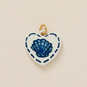 Detalle de colgante de corazón de cerámica blanca con dibujo de concha azul y aro dorado
