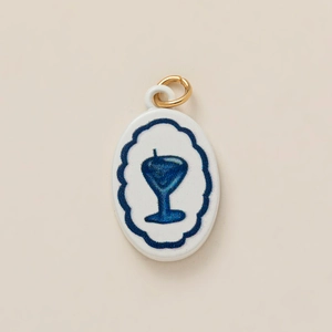 Detail of oval white enamel jewelry pendant featuring a blue cocktail glass design