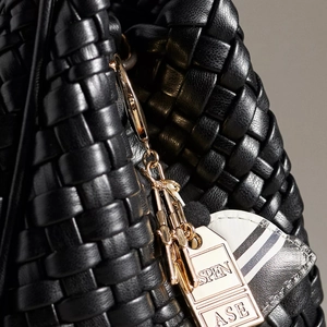 Close-up of black woven leather handbag detail with premium gold hardware and charm