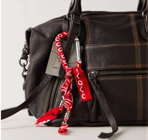 Detailed close-up of dark brown textured leather bag with red fabric keychain and silver clip