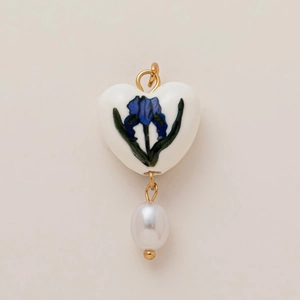 Dettaglio del ciondolo a cuore in ceramica bianca con motivo floreale blu e perla dorata