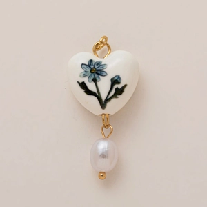 Dettaglio del ciondolo a cuore in ceramica bianca con fiori blu e perla barocca