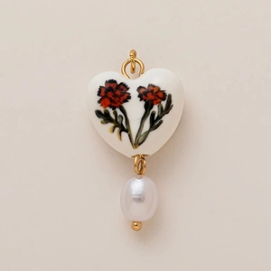 Dettaglio di un ciondolo a cuore in ceramica con fiori dipinti a mano e una perla