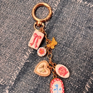 Détail de porte-clés doré avec breloques papillon, fleur et cœur roses sur fond de denim