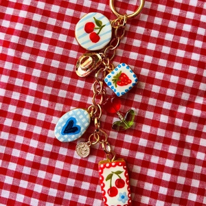 Porte-clés doré avec breloques fruits et mini chapeau sur tissu à carreaux rouge et blanc