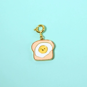 Macro detail of toast and smiling fried egg enamel pendant with golden lobster clasp