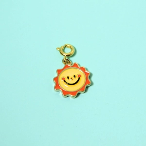 Detail of colorful sun charm with yellow smiling face and orange enamel coating