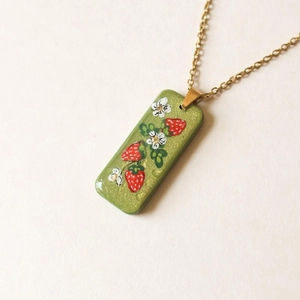 Detail of a gold-plated flower pendant with red strawberries on green resin