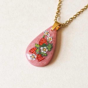 Detail of pink teardrop pendant with painted strawberry and flowers on a gold chain