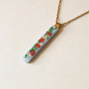 Detailed view of rectangular light blue pendant with red strawberry and gold chain