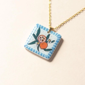 Close-up of a square floral pendant necklace with orange motif and 18K gold plated chain