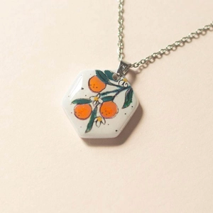 Detail of hexagon pendant with hand-painted orange fruit illustration on 18K gold chain