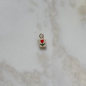 Detalle de un colgante cuadrado con motivo de tulipán rojo sobre fondo de mármol blanco
