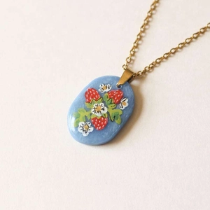Detailed macro view of hand-painted strawberry pattern on blue oval pendant with gold chain