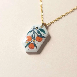 Macro detail of hexagonal ceramic pendant featuring hand-painted orange branch on gold chain