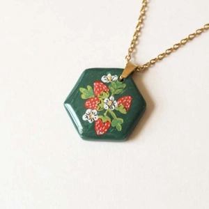 Macro shot of 18K gold plated hexagonal strawberry pendant with green floral motifs