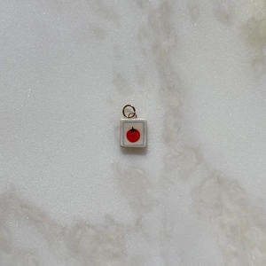 Detalle de colgante cuadrado con diseño de tomate rojo y aro metálico en acabado dorado