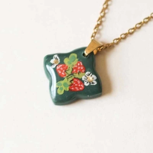 Detail of flower and strawberry printed square pendant on a golden chain necklace