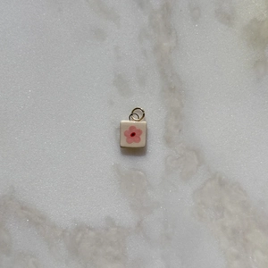 Vista macro de un colgante cuadrado de esmalte con diseño floral rosa sobre mármol