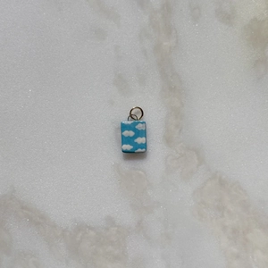 Detalle macro del colgante de esmalte azul cielo con patrón de nubes blancas en acero