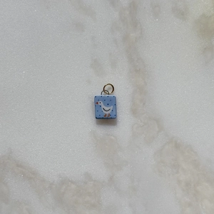 Detalle de un colgante cuadrado de esmalte azul claro con un ganso blanco sobre fondo de mármol