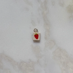 Detalle de un colgante cuadrado de acero inoxidable con motivo de fresa y anillo dorado