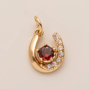 Détail d'un pendentif fer à cheval doré avec pierre précieuse rouge et zircons blancs