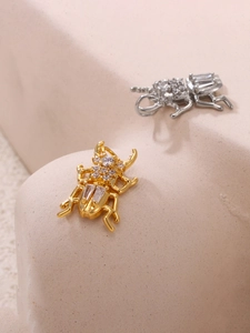 Dettaglio di ciondoli a scarabeo in oro e argento con fitti cristalli di zircone micro-pave
