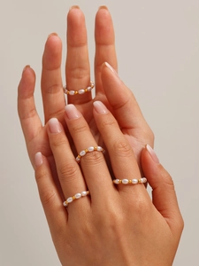 Dettaglio di anelli a fascia con perle e sfere dorate sovrapposti in stile minimalista