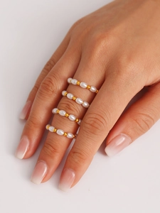 Dettaglio di quattro anelli di perle minimalisti con perline dorate sulla mano della modella