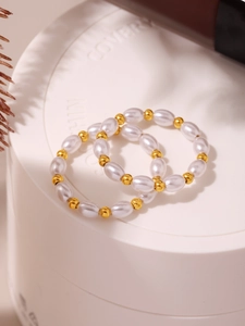 Dettaglio del set di anelli con perle bianche e perline metalliche dorate lucide