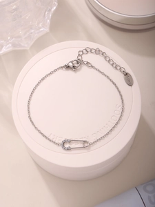 Detailaufnahme eines Armbands aus Edelstahl mit funkelndem Sicherheitsnadel-Anhänger