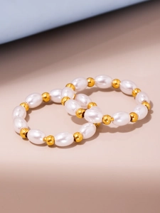 Primo piano di anelli eleganti con perle bianche e perline dorate su sfondo beige