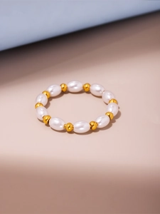 Dettaglio di perle bianche ovali e perle cilindriche dorate su un anello elastico