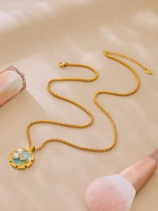 Dettaglio collana vintage dorata con ciondolo in smalto blu floreale e perla di conchiglia