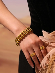 Détail d'un bracelet à double rangée de perles dorées et de bagues sur velours noir