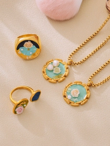 Dettaglio macro della collana e degli anelli con rose in smalto vintage e perle dorate