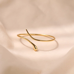 Minimalistische gouden slangenarmband met groene edelsteen op linnen achtergrond