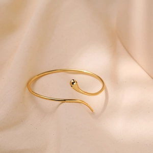 Minimalistische gouden slangenarmband met groene ogen op een zijden achtergrond