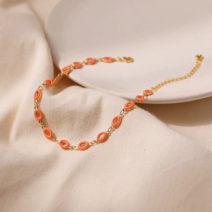 Detail der Gold-Fußkette mit orangefarbenen Emaille-Anhängern und verstellbarem Verschluss