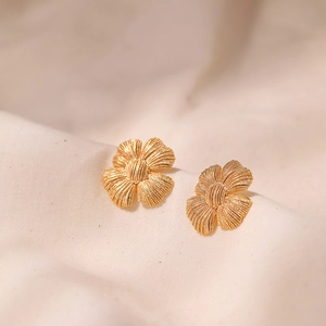 Macro detail of 18K gold plated flower earrings showing realistic petal texture on linen fabric