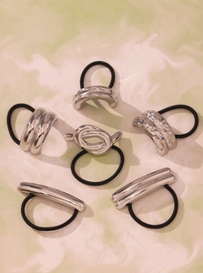 Detail view of six geometric silver metal elastic hair ties on green marble texture