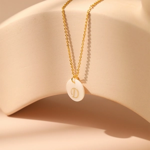 Gros plan d'un collier doré avec pendentif disque en nacre blanche orné de la lettre D