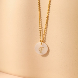 Vue macro du collier plaqué or 18K montrant le pendentif en nacre avec la lettre F