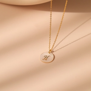 Gros plan d'un collier doré avec la lettre H gravée sur un pendentif en nacre