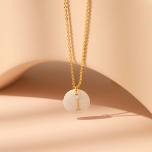 Détail macro du pendentif en nacre naturelle avec la lettre I dorée sur chaîne fine
