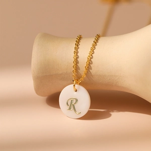 Détail du collier plaqué or 18K montrant un pendentif en nacre avec la lettre R dorée