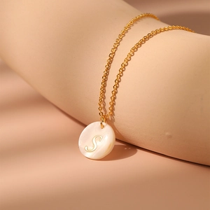 Gros plan d'un pendentif en nacre avec lettre S dorée sur une chaîne minimaliste en laiton
