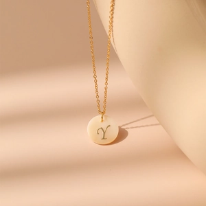 Détail macro de la lettre Y gravée sur un pendentif en nacre et chaîne dorée