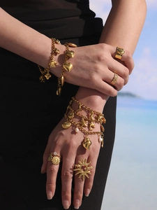 Detalle de pulseras de amuletos doradas y anillos con motivos de conchas y elefantes